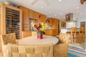 A modern kitchen with wooden cabinets, a central island, and a dining area with wicker chairs and a round table.