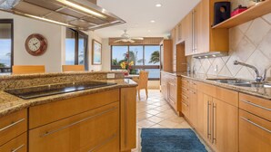 Una cocina moderna con armarios de madera, encimeras de granito, horno integrado y un amplio ventanal con vistas a palmeras.