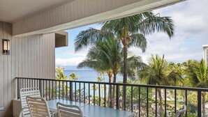 Un balcone con tavolo e sedie, vista su una palma e l'oceano.