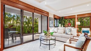 A spacious living area with a large sliding glass door leading to a balcony, a round coffee table, and a comfortable seating arrangement. - Modern Beach Condo with Platinum Rating (Lahaina)