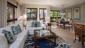 A spacious living room with a sofa set, a glass coffee table, and a dining area with wicker chairs.