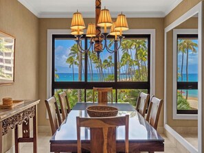 Ein Essbereich mit Blick auf Palmen und das Meer, eine Chandelier und ein Tisch mit Stühlen.