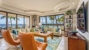 Een ruime woonkamer met een groot raam met uitzicht op een strand, ingericht met lederen fauteuils, een bank en een salontafel.