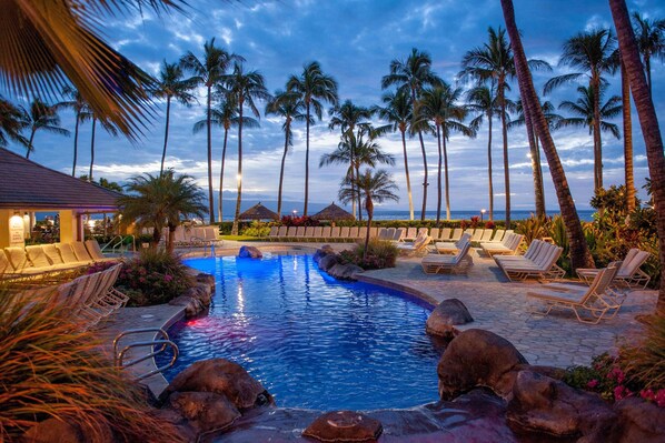 Relax by the serene pool surrounded by palm trees and lounge chairs.