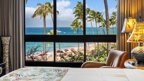 Ein Hotelzimmer mit großem Fenster und Blick auf Strand, Palmen und Meer.