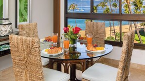 Tavola imbandita con croissant, frutta e succo d'arancia, con vista su una spiaggia con palme e barche.
