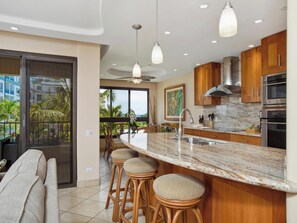 A modern kitchen with a marble countertop, wooden cabinets, stainless steel appliances, and a bar area with stools.