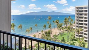 A balcony with a view of a beach, palm trees, and a building with balconies overlooking the ocean.