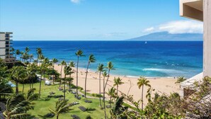 A beach view with palm trees, a clear sky, and a distant mountain. - Panoramic Ocean Views | 3BR Sleeps 6 w/ Private Lanai (Lahaina)