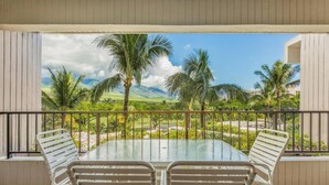 A balcony with a glass table and metal chairs, overlooking a tropical landscape with palm trees and mountains. - Kaanapali Alii 455 | Hot Tub | Pool | Sunrise Views (Lahaina)
