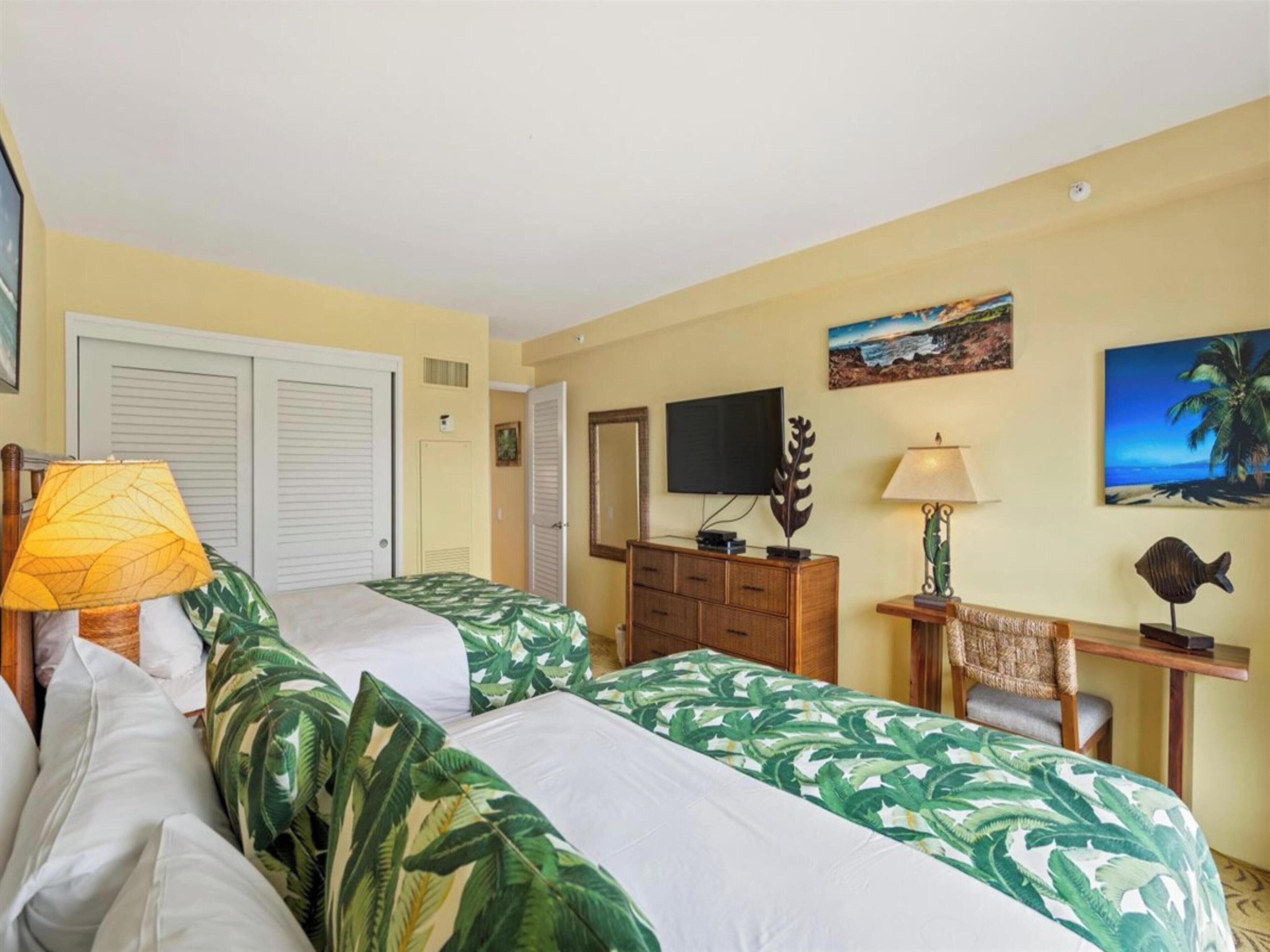 A hotel room with two beds, a television, a desk with a chair, and artwork on the walls.