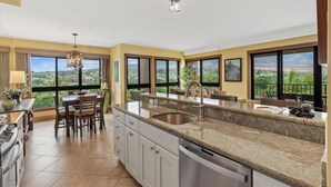A spacious kitchen with a large island, a dining area, and a view of the landscape. - Mountain, Golf, and Sunrise Views - Kaanapali Alii 475 (Lahaina)