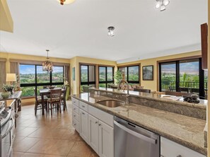 A spacious kitchen with a large island, a dining area, and a view of the landscape. - Mountain, Golf, and Sunrise Views - Kaanapali Alii 475 (Lahaina)