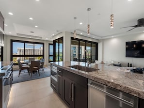 A modern kitchen with a large island, dark cabinetry, and a view of a balcony.