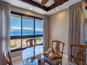 Un coin repas avec une table en verre, des chaises en osier et une vue sur la plage.
