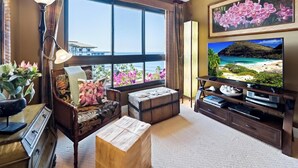 A living room with a large window, a television, and a sofa with floral cushions.