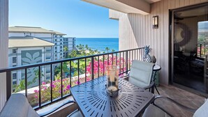 A balcony with a table, chairs, and a view of the ocean and buildings.