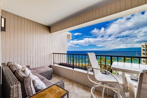 Enjoy the ocean view from this balcony with a wicker sofa set and a chair.