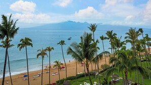 Una playa con palmeras, orilla arenosa y vista al océano y montañas a lo lejos.