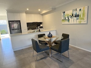 A modern kitchen with a dining area, featuring a glass table and chairs, a refrigerator, and a microwave. - Merchant's Court: Central and Quiet 3 bedroom townhouse! (Wangaratta)