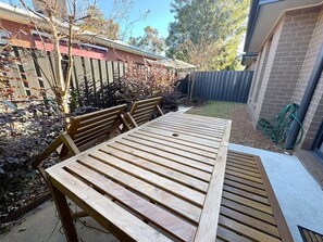 A wooden table and benches in a backyard with a brick wall and a wooden fence. - Merchant's Court: Central and Quiet 3 bedroom townhouse! (Wangaratta)