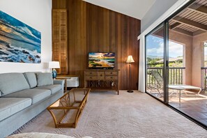 Relax in this stylish living room with a large flat-screen TV, comfortable sofa, and a floor lamp. Enjoy the view from the sliding glass door leading to the outdoor patio.