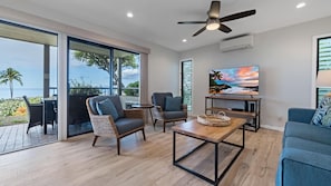 Enjoy the ocean view from the large window in this living room, featuring a flat-screen TV and comfortable sofa.