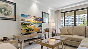 A modern living room with a large flat-screen TV, a sofa, a coffee table, and a lamp.