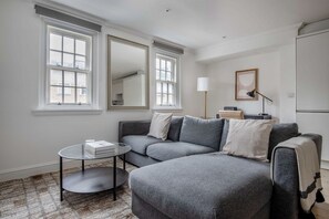 A modern living room with a grey sectional sofa, a glass coffee table, and a large mirror. - Open Waterloo 2BR, nr London Eye, Museums & Station, by Blueground (London)