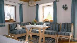 Een gezellige kamer met een hoekbank, een houten tafel en een raam met gordijnen.