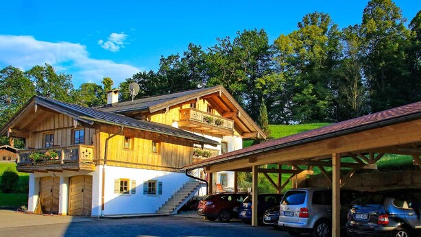 Een houten chalet met balkon, een overdekte parkeerplaats en een trap naar de ingang.