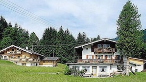 Een chalet met meerdere verdiepingen en een balkon, omringd door weelderig groen en bomen.