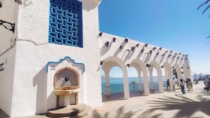 A white building with blue window shutters and a covered outdoor seating area. - Nerja Sun Apartments Casa Cipreses 5 (Nerja)
