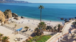 A beach with clear blue water, palm trees, and a rocky cliff. - Nerja Sun Apartments Casa Cipreses 5 (Nerja)
