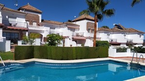 A swimming pool with a tiled edge, surrounded by white buildings with red-tiled roofs and balconies. - Nerja Sun Apartments Casa Cipreses 5 (Nerja)