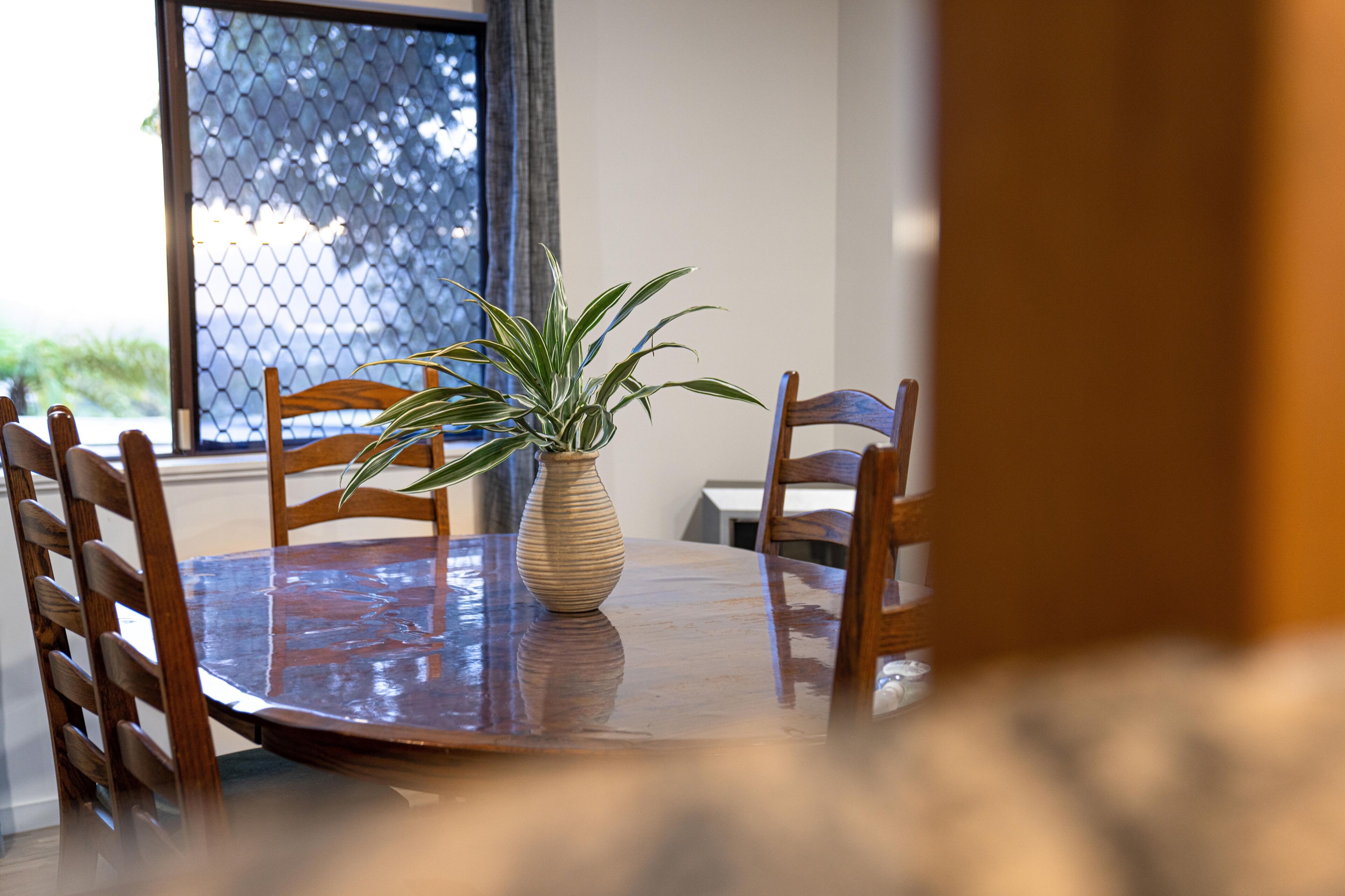 A round wooden dining table with a potted plant in the center, surrounded by wooden chairs.