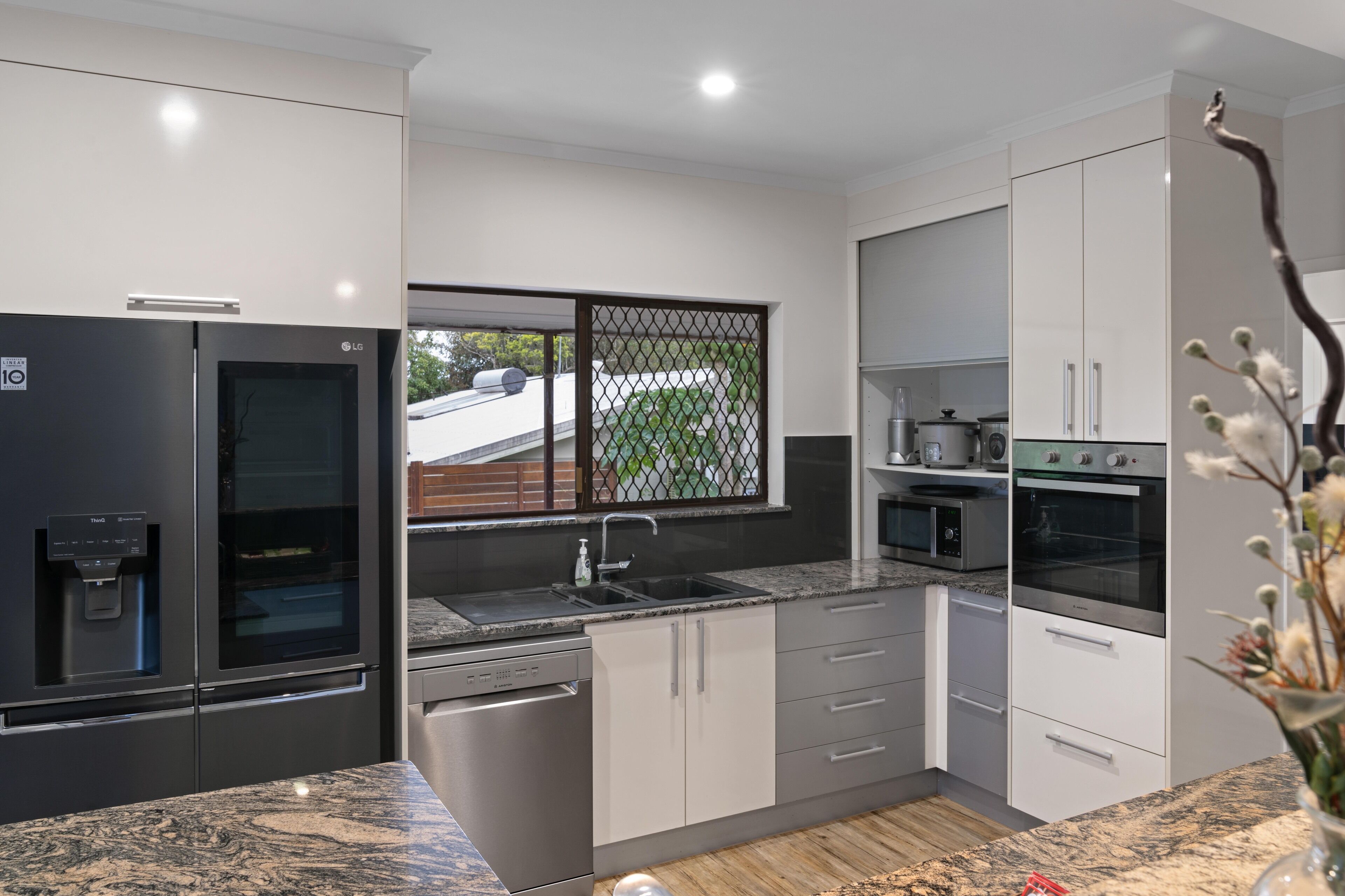 A modern kitchen with a built-in refrigerator, oven, and dishwasher, featuring a granite countertop and white cabinetry.
