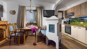 A cozy kitchen with wooden cabinets, a dining area with a table and chairs, a television, and a window with curtains. - Vacation apartment Hirscherl, 1-2 persons, 55 sqm (Schönau am Königssee)