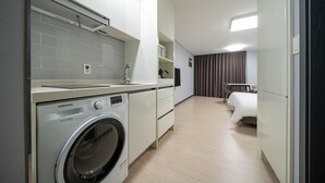 Ein modernes Hotelzimmer mit Waschmaschine, einem Bett, einem kleinen Tisch und einem Stuhl.