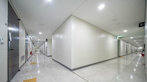 Ein langer, gut beleuchteter Korridor mit Fliesenboden, Notausgangsschildern und einem Feuerlöscher an der rechten Wand.
