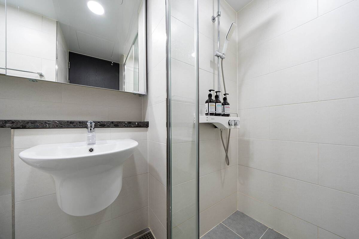 Un baño con lavamanos blanco, cabina de ducha de vidrio y espejo sobre el lavamanos.