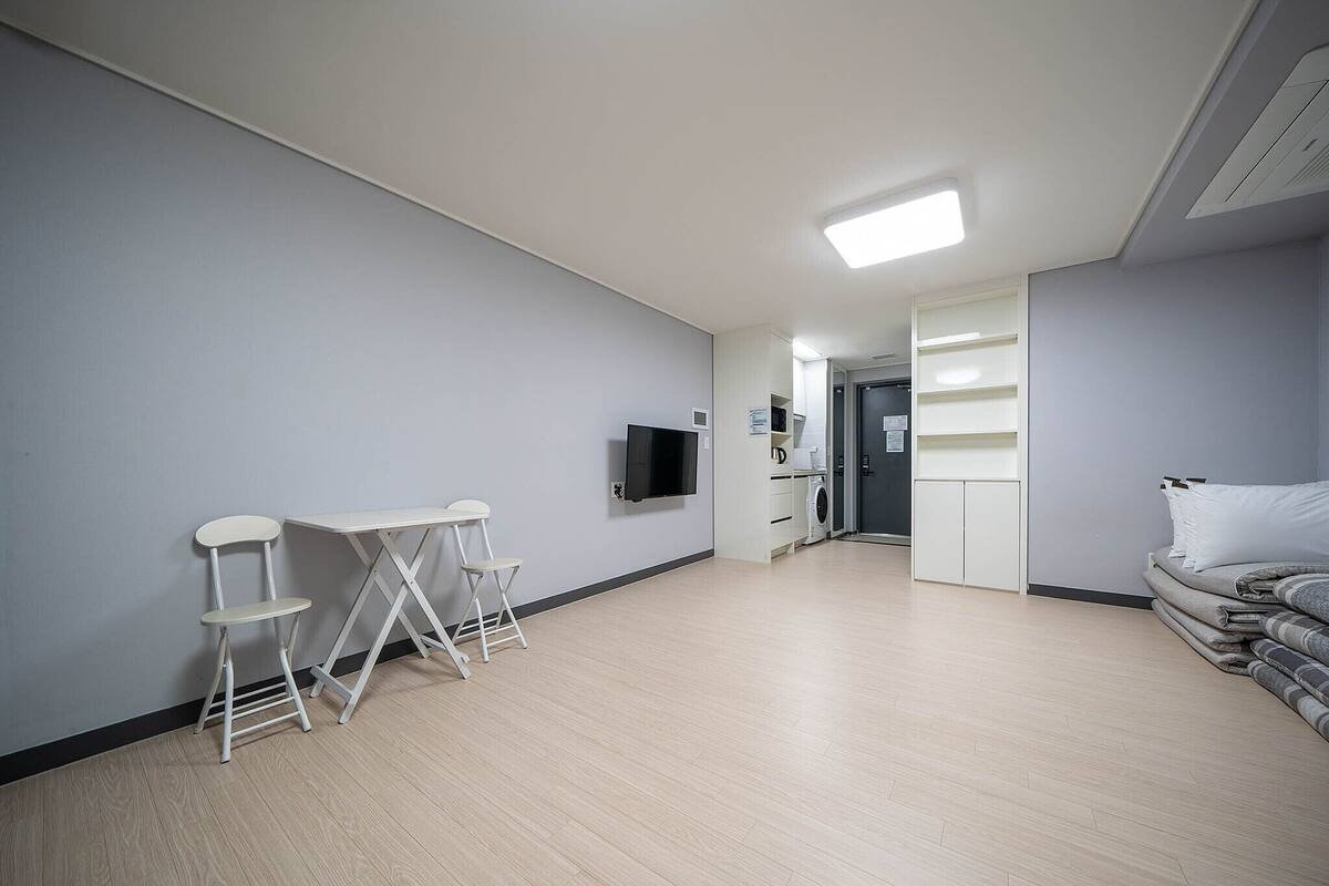 Una habitación moderna y luminosa con televisión de pantalla plana, una pequeña mesa con sillas, un sofá y un armario.