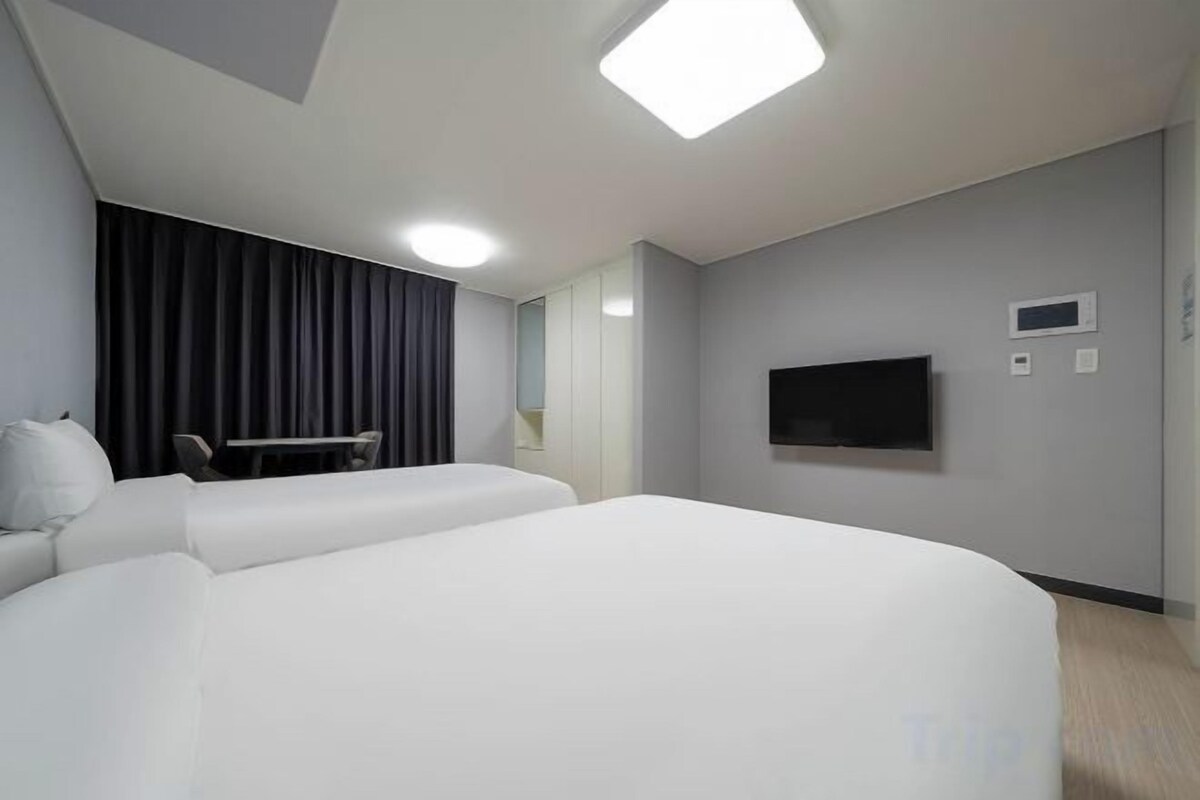 Une chambre d’hôtel avec un grand lit, un bureau, une chaise, un téléviseur à écran plat et des rideaux occultants.
