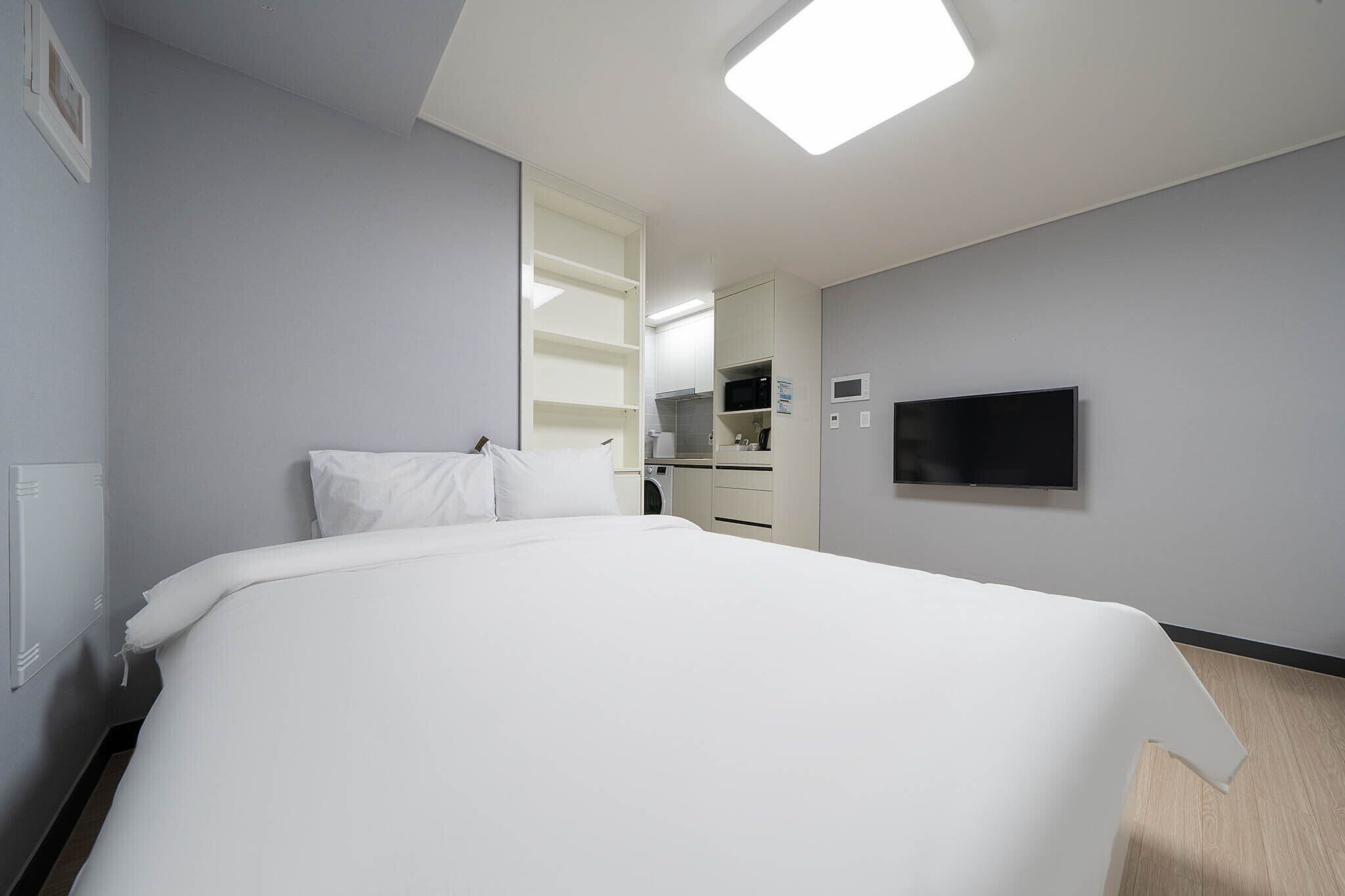 Hotellihuone, jossa on suuri sänky, seinälle asennettu taulutelevisio ja pieni keittiönurkkaus.