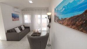 Ein Wohnzimmer mit grauem Sofa, einem kleinen runden Tisch, einer Stehlampe und einem großen Landschaftsbild an der Wand.