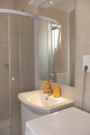 Une salle de bain avec une douche Ă parois de verre, un lavabo avec un miroir et un distributeur de savon jaune.