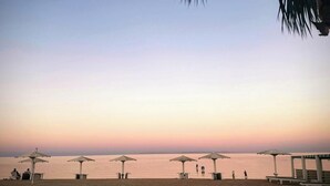 A beach with several umbrellas and lounge chairs, a clear sky, and a calm sea.
