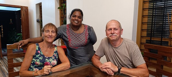 Tres personas sentadas en una mesa de madera en una habitación con una ventana y una puerta.