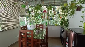 Uma área de refeições com mesa e cadeiras, uma máquina de lavar e diversos vasos com plantas.