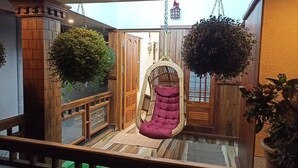 Uma cadeira suspensa numa varanda com piso de madeira, plantas em vasos e vista para o exterior.